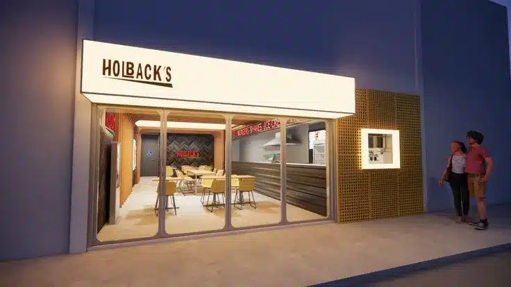 Fachada comercial pequena da Holback's com iluminação noturna e clientes na calçada